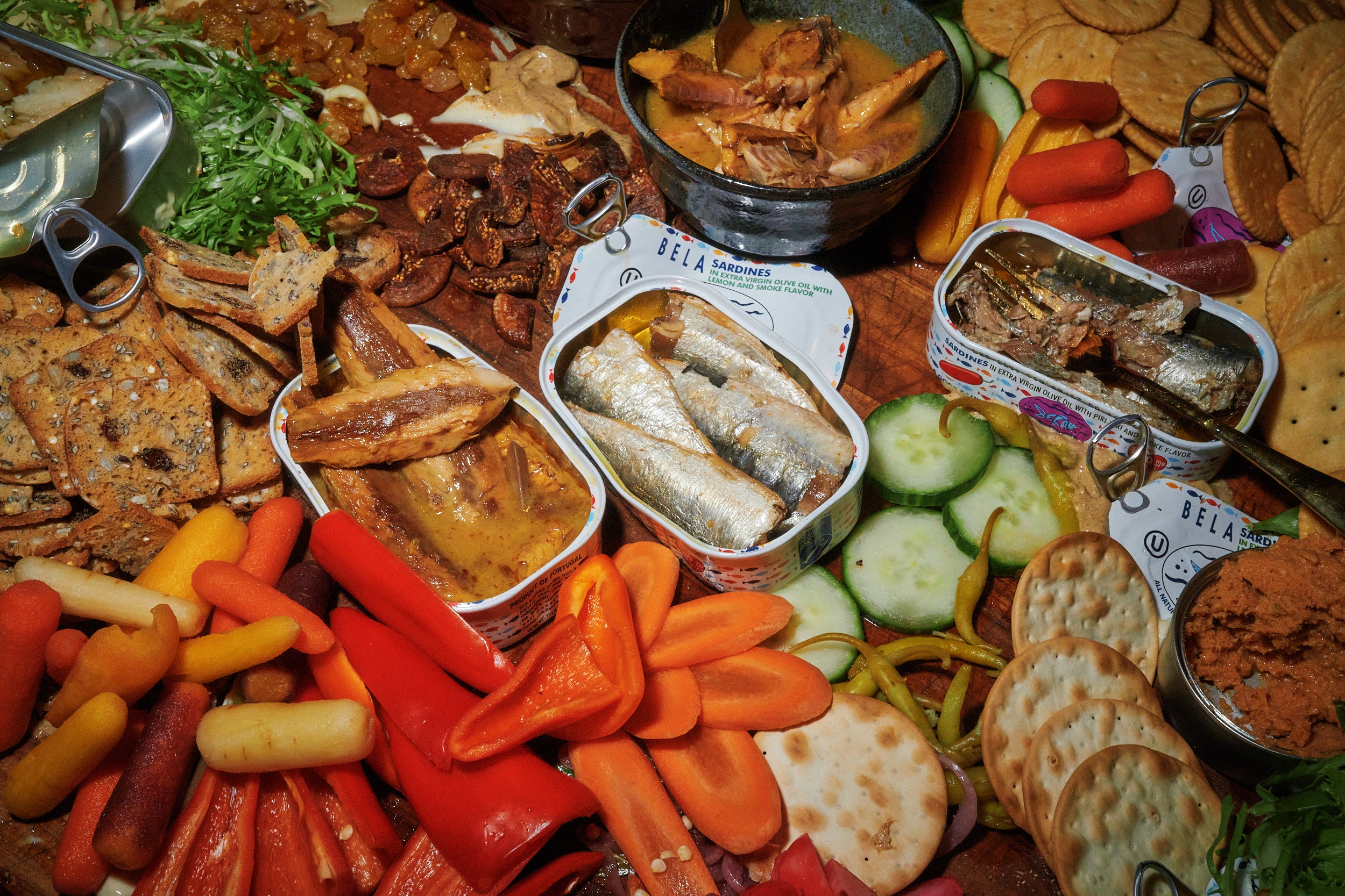 Open BELA tins next to crackers and assorted vegetables